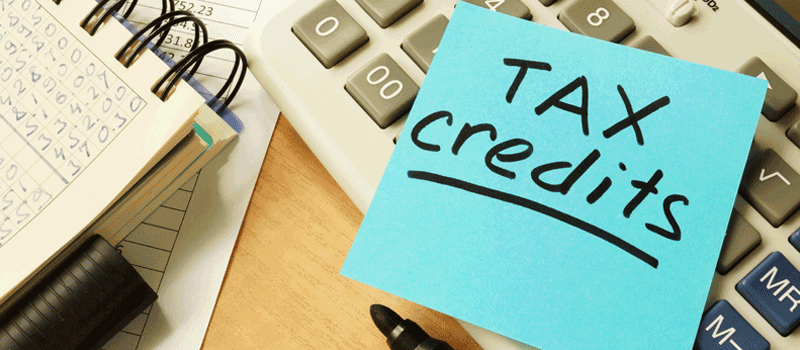the words tax credit written on sticky note on top on calculator and tax paperwork